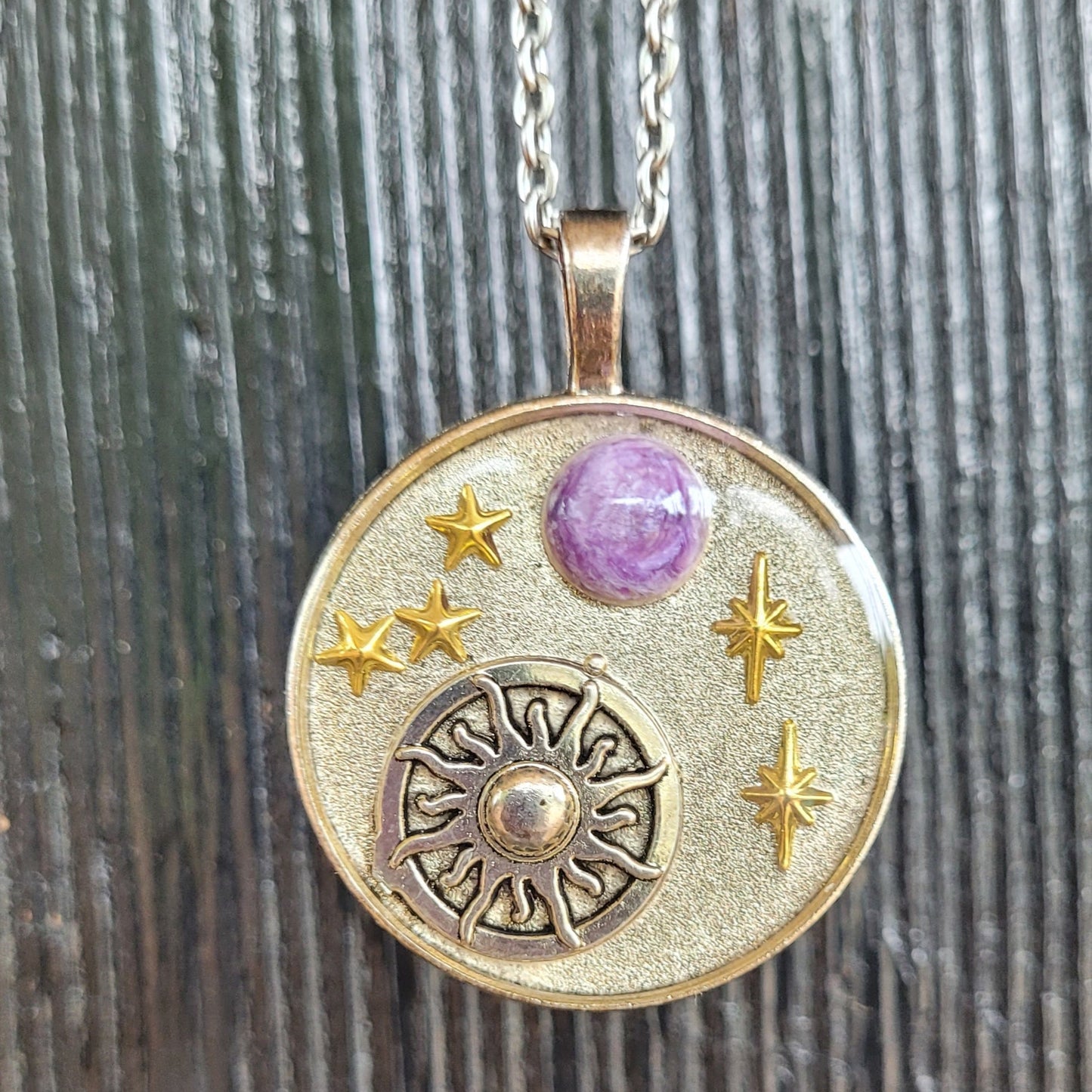 Silver pendant with purple gemstone and star designs on a wooden background