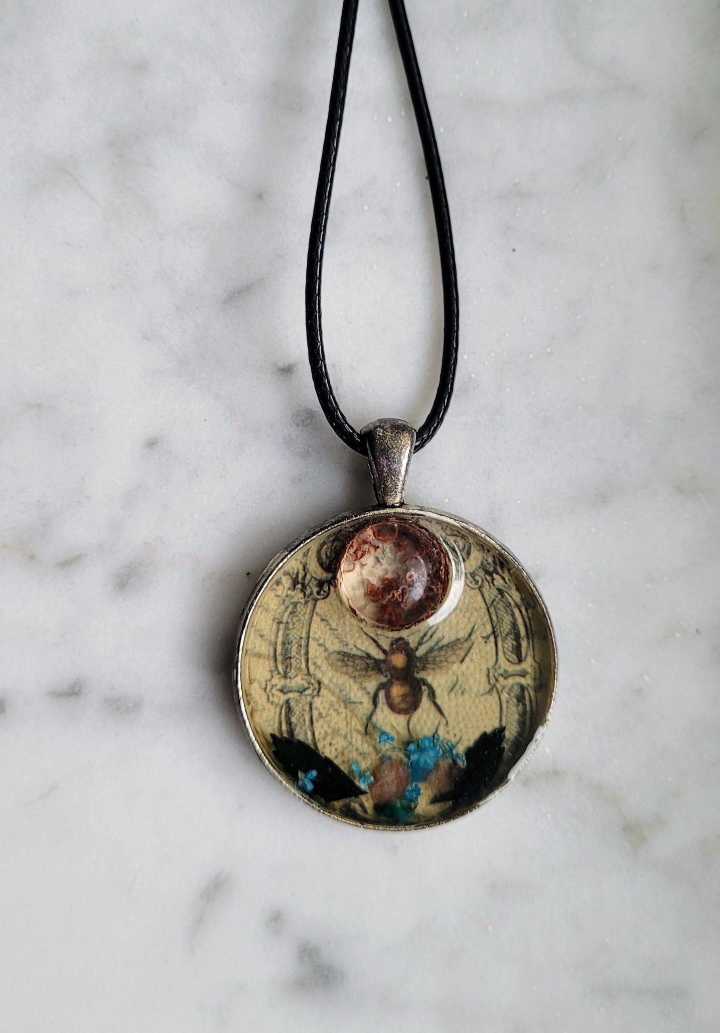 Necklace with a round pendant featuring a bee design on a marble surface
