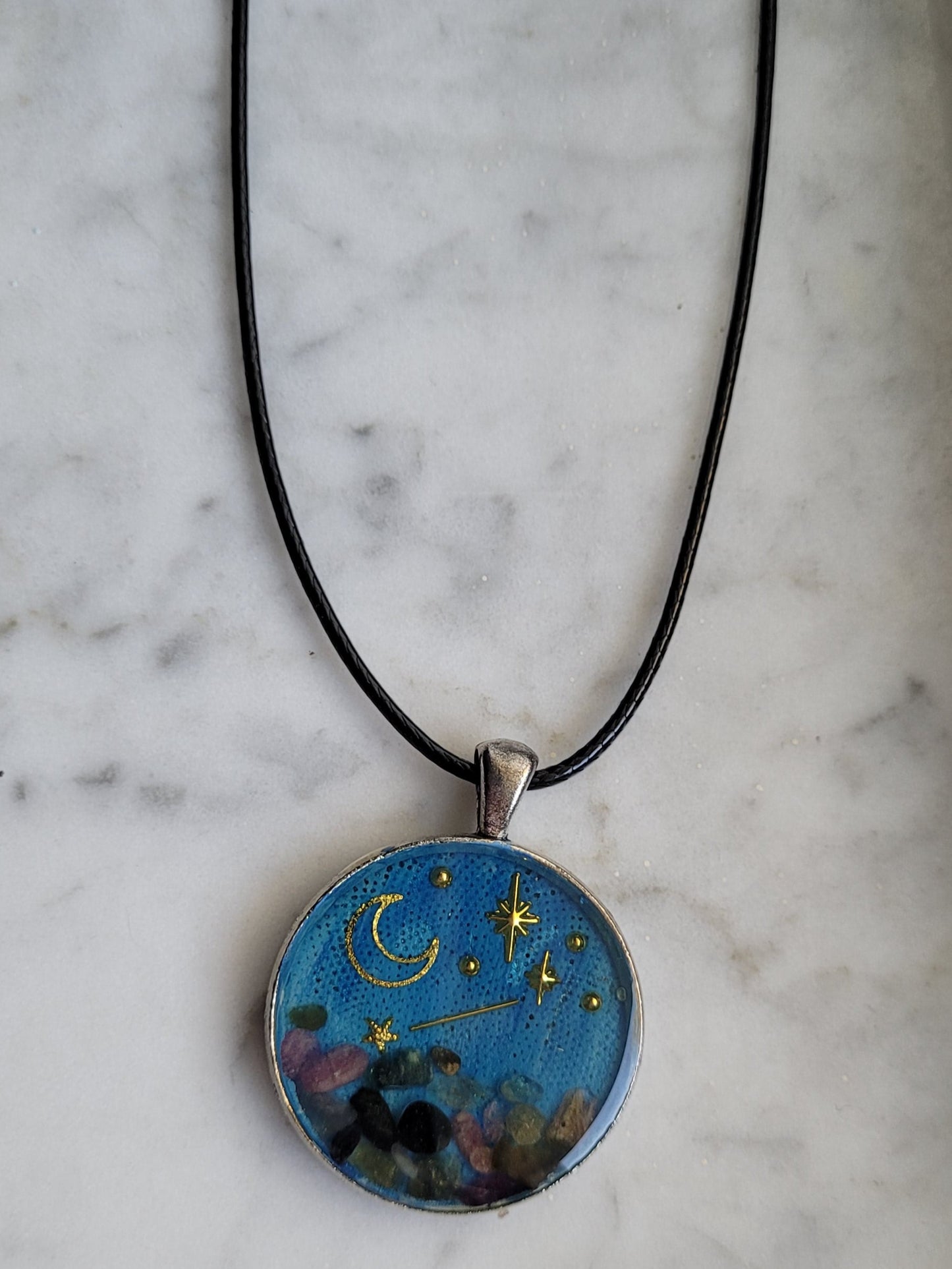 Round pendant with celestial design on a black cord against a marble background