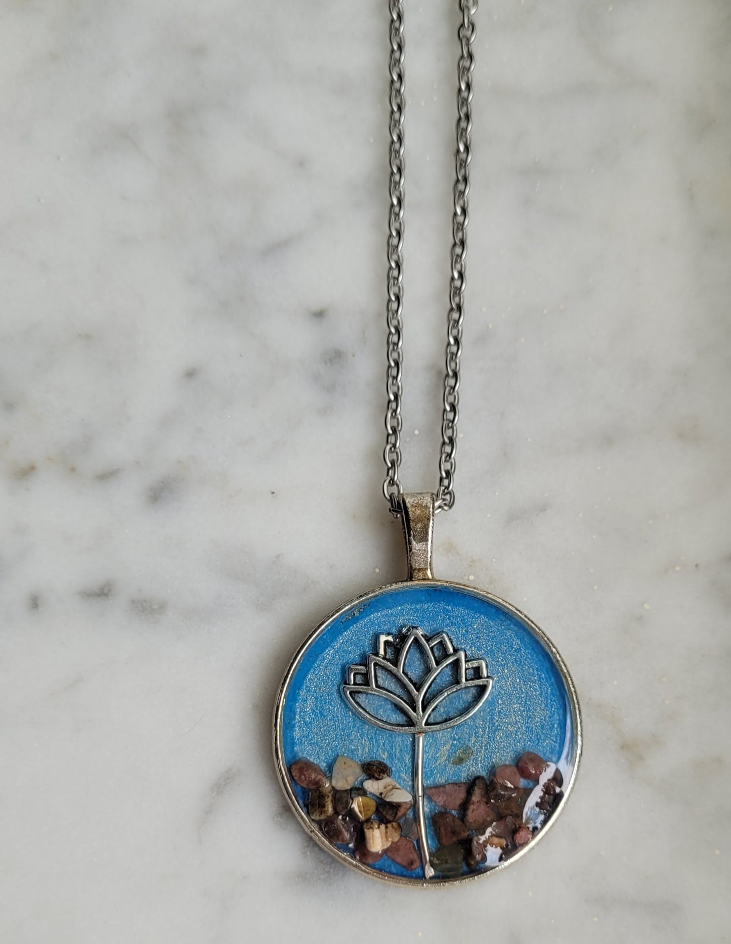 Necklace with a round pendant featuring a lotus flower design on a marble surface