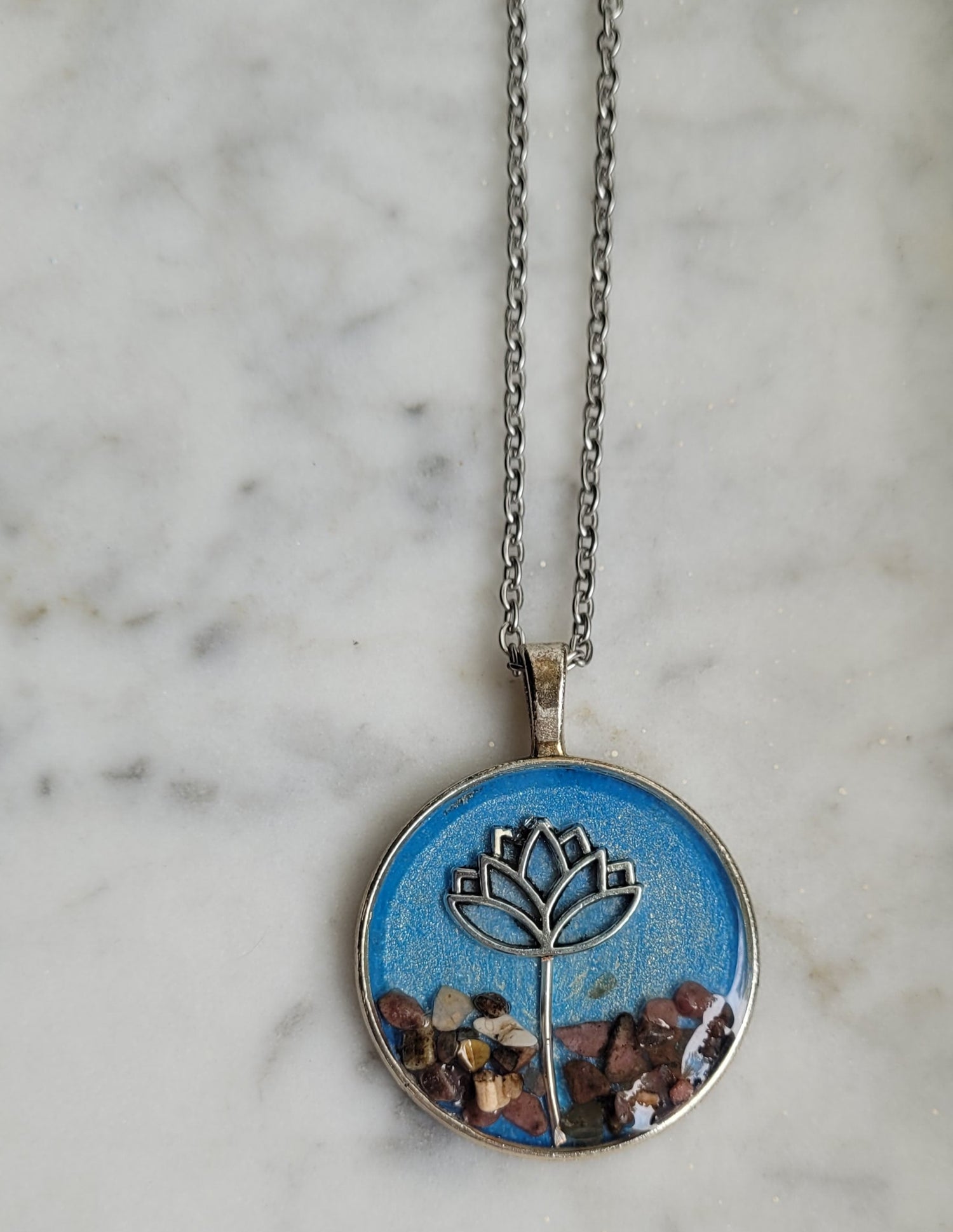Necklace with a round pendant featuring a lotus flower design on a marble surface