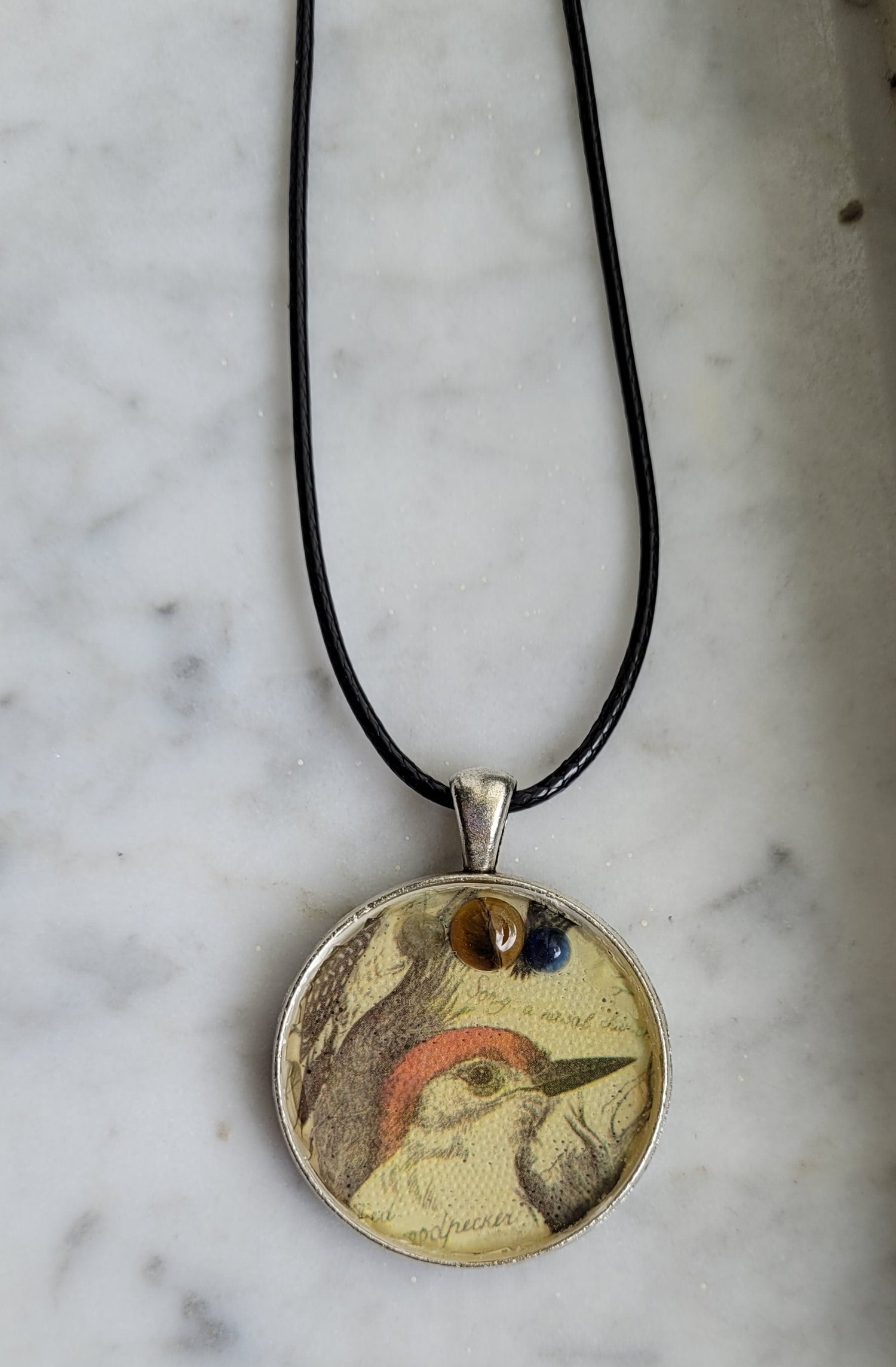 Necklace with a round pendant featuring a woodpecker colorful design on a marble surface