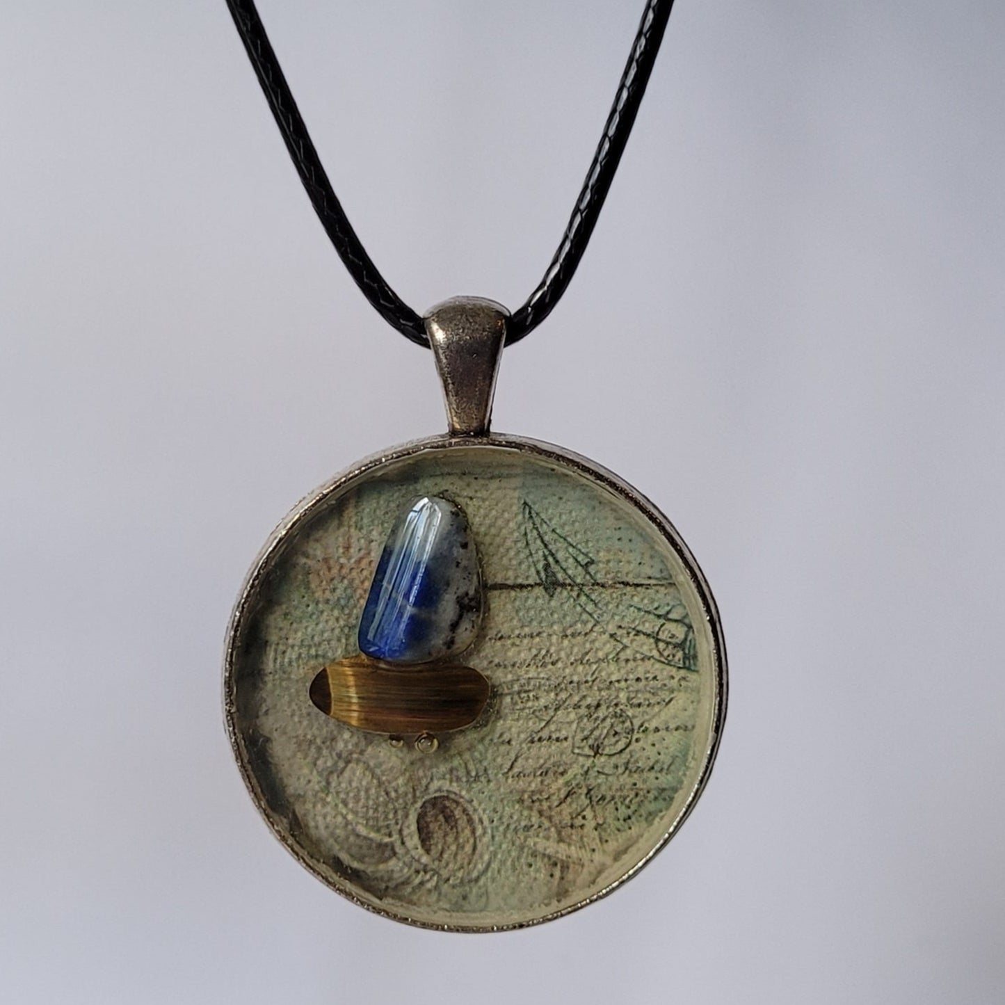 Round pendant with a blue stone on a black cord against a white background