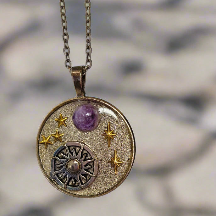 Necklace with a circular pendant featuring stars and a purple gemstone on a textured surface.
