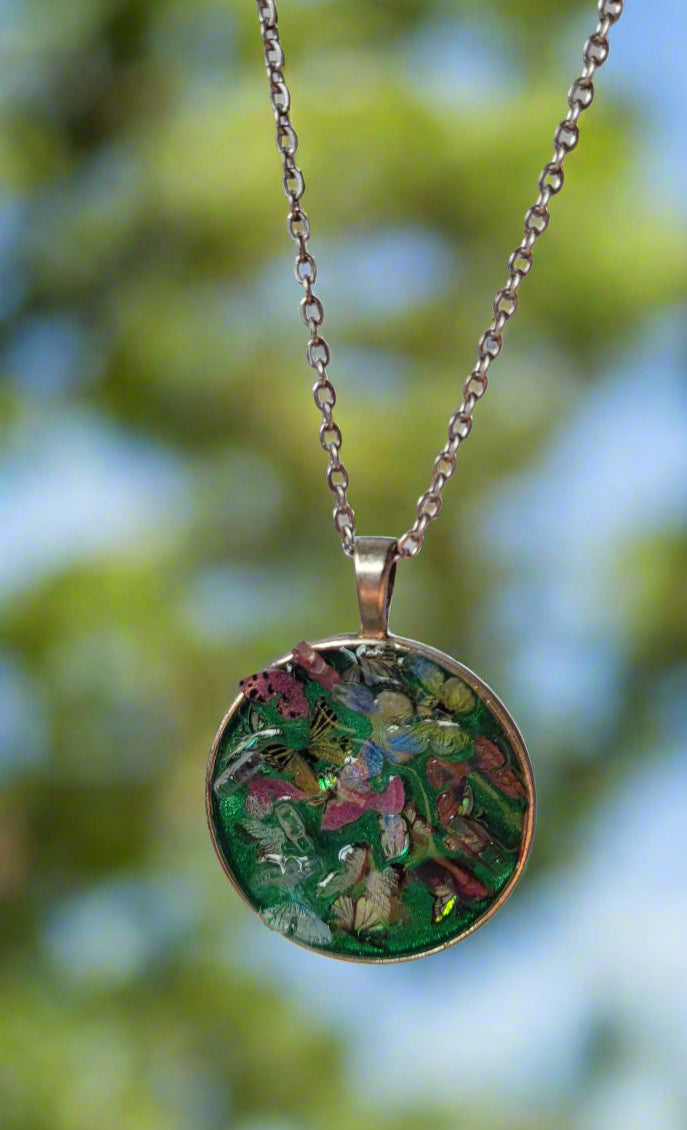 Necklace with a round pendant featuring green and pink butterflies against a blurred natural background