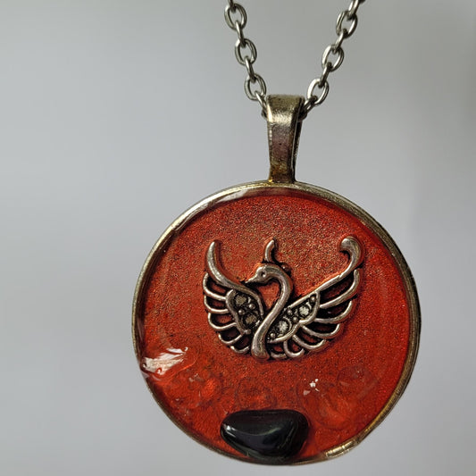 Round pendant with phoenix design on a chain against a neutral background